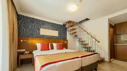 Hotellihuone, jossa kaksi sänkyä, koristeellinen tapetti ja kierreporras ylös. (Tekoälyn luoma teksti)
