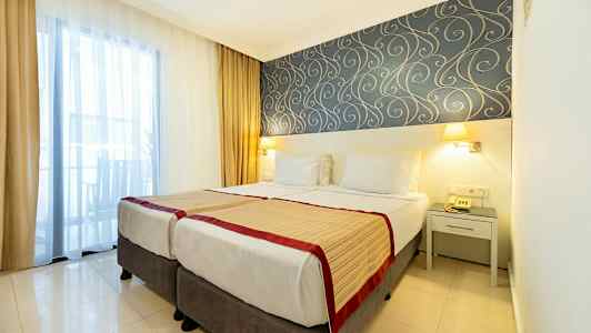 Hotellihuone kahdella yhden hengen vuoteella, koristeelliset tapetit ja ikkunassa verhot. (Tekoälyn luoma teksti)