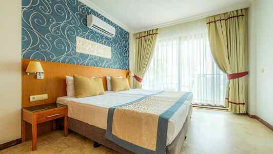 Hotellihuone, jossa on parivuode, sinistä ja kullanväristä sisustusta sekä ikkuna vaaleilla verhoilla. (Tekoälyn luoma teksti)