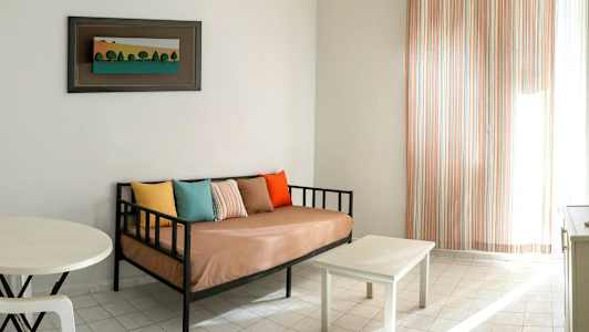 Olohuone, jossa on sohva, erivärisiä tyynyjä, pieni pöytä ja taulu seinällä. (Tekoälyn luoma teksti)