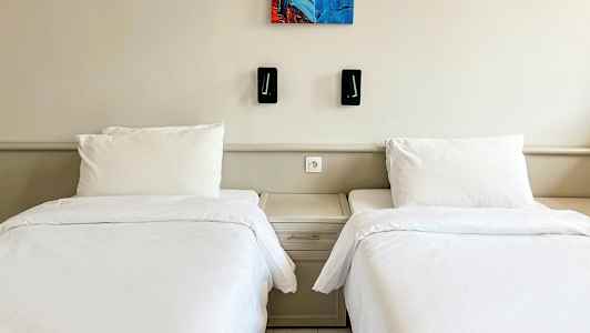 Kaksi yhden hengen vuodetta valkoisilla vuodevaatteilla ja yhteinen yöpöytä niiden välissä. (Tekoälyn luoma teksti)