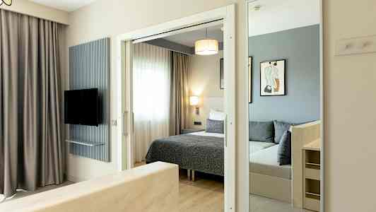 Kuva hotellihuoneesta, jossa on sänky, peili ja televisio. (Tekoälyn luoma teksti)