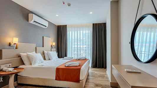 Hotellihuone, jossa on parivuode, yöpöytä, koristeellinen peili seinällä ja ikkunat verhoilla. (Tekoälyn luoma teksti)