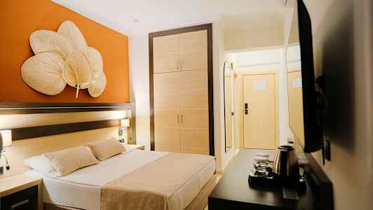 Hotellihuone, jossa on sänky, vaatekaappi ja oranssi seinäkoriste. (Tekoälyn luoma teksti)