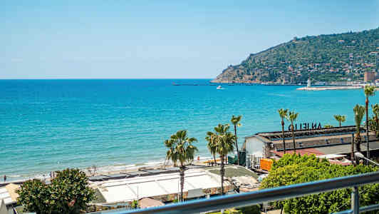 Näkymä merelle ja rannalle, jossa on rakennuksia etualalla. Taustalla näkyy niemimaa, jolla on asutusta. (Tekoälyn luoma teksti)