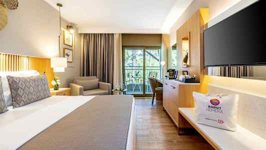 Hotellihuone, jossa on mukava sänky, nojatuoli, istuinryhmä parvekkeella ja nykyaikaiset kalusteet. (Tekoälyn luoma teksti)