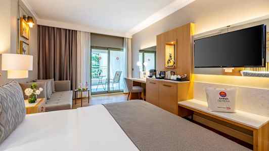 Hyvin sisustettu hotellihuone, jossa on parivuode, istuinryhmä, työpöytä ja parveke. (Tekoälyn luoma teksti)