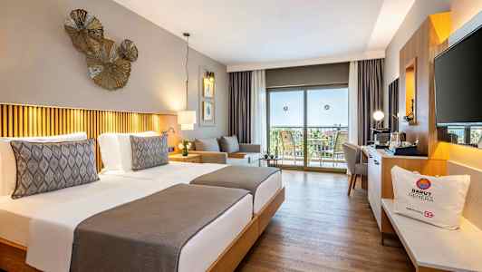 Hotellihuone, jossa on kaksi yhden hengen vuodetta, koristeellinen valaistus ja näkymä parvekkeelle, jossa on kalusteita. (Tekoälyn luoma teksti)