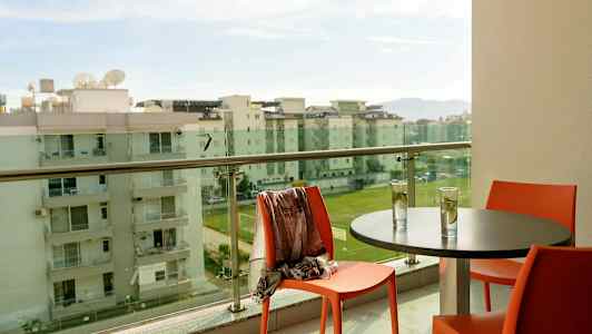 Parveke, jossa istuimet, pöytä kahdella lasilla ja näkymä hotellirakennuksiin. (Tekoälyn luoma teksti)