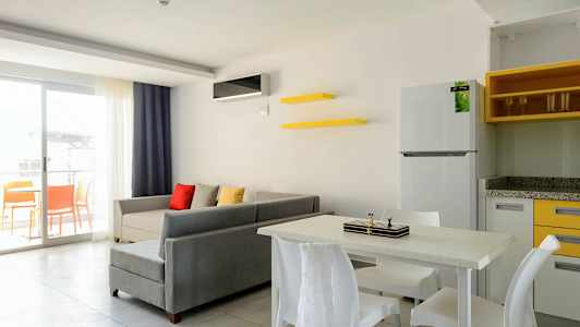 Olohuone harmaalla sohvalla, värikkäillä tyynyillä, ruokapöytä tuoleineen ja avoin parveke. (Tekoälyn luoma teksti)