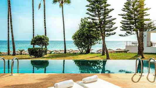 Rannalla sijaitseva uima-allas, aurinkotuoleja ja ympäröiviä palmuja. (Tekoälyn luoma teksti)