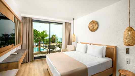 Hotellihuone, jossa suuri sänky ja parveke, josta näkyy uima-allas ja palmupuita. (Tekoälyn luoma teksti)