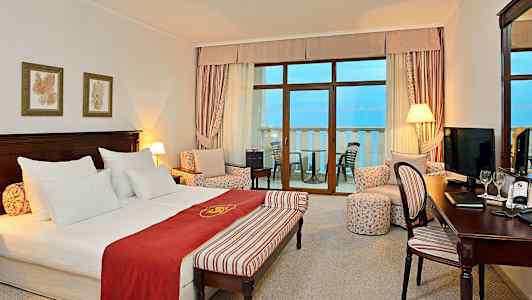 Hotellihuone, jossa parivuode, istuinryhmä ja parveke merinäkymällä. (Tekoälyn luoma teksti)