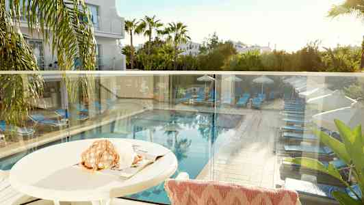 Näkymä terassilta, jossa näkyy uima-allas, aurinkovuoteita ja aurinkovarjoja vehreyden ympäröimänä. (Tekoälyn luoma teksti)