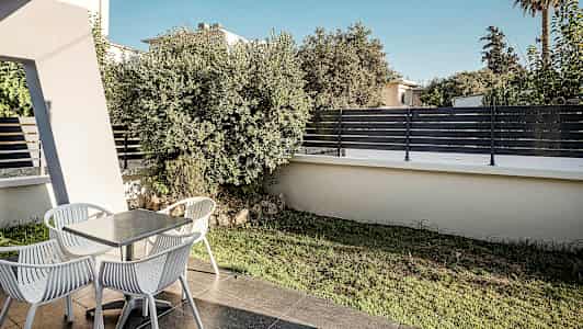 Terassi, jossa on pöytä ja neljä tuolia, ympäröitynä kasvillisuudella ja aidalla. (Tekoälyn luoma teksti)