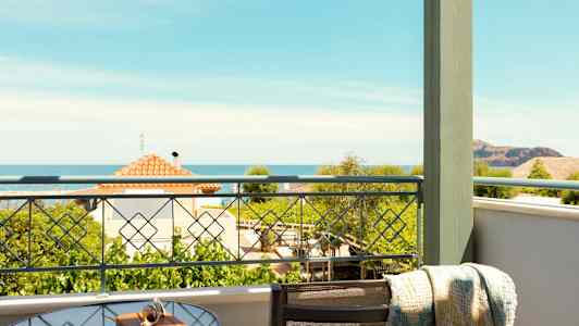 Näkymä parvekkeelta, jolla on lasipöytä ja tuoli. Taustalla näkyvät meri ja talot. (Tekoälyn luoma teksti)