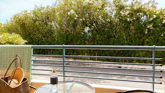 Näkymä parvekkeelta, jossa on lasipöytä, tuolit ja vehreää kasvillisuutta taustalla. (Tekoälyn luoma teksti)