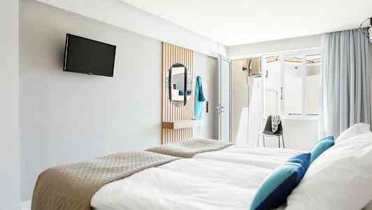 Hotellihuone, jossa vuoteet, TV seinällä ja peili. (Tekoälyn luoma teksti)