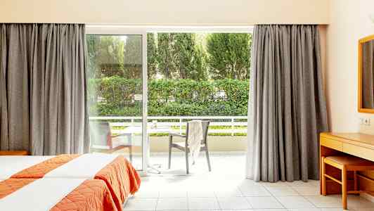 Hotellihuone, jossa on kaksi erillistä vuodetta ja suuri ikkunallinen ovi, joka johtaa parvekkeelle. (Tekoälyn luoma teksti)