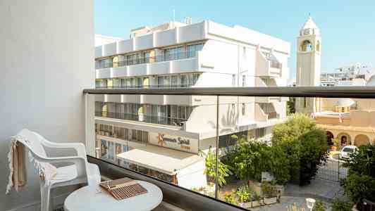 Näköala parvekkeelta, jossa pöytä ja tuoli, taustalla rakennus ja kirkontorni. (Tekoälyn luoma teksti)