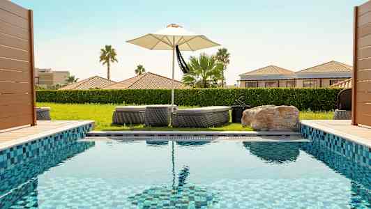 Uima-allas, taustalla aurinkotuoleja ja aurinkovarjo. (Tekoälyn luoma teksti)