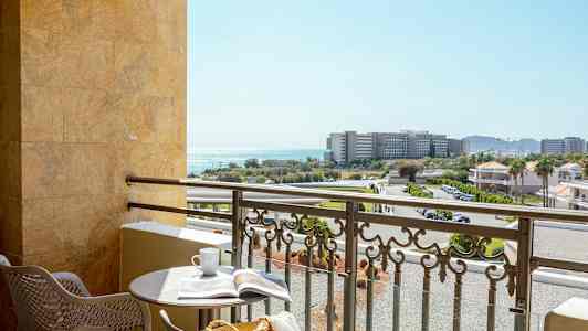 Parveke, jossa pyöreä pöytä, kaksi tuolia ja näkymä rakennuksiin, teille ja merelle. (Tekoälyn luoma teksti)