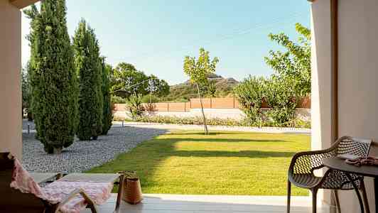 Näkymä terassilta, jossa on tuoleja ja pöytä, nurmikko ja puita taustalla. (Tekoälyn luoma teksti)