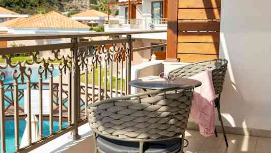 Parveke, jossa kaksi istumapaikkaa, pieni pöytä ja kaunis näkymä uima-altaalle ja rakennuksille. (Tekoälyn luoma teksti)