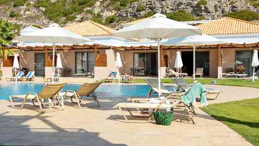 Aurinkotuoleja uima-altaan äärellä bungaloweja ja puutarha taustalla. (Tekoälyn luoma teksti)