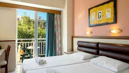 Hotellihuone, jossa on parisänky, lukuvalot, kirjoituspöytä ja parveke, josta on näkymä vehreään ympäristöön. (Tekoälyn luoma teksti)