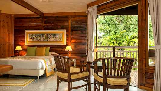 Puupaneloitu makuuhuone, jossa on parivuode, kaksi tuolia ja pöytä, suureen avaukseen päin parvekkeelle, jolta on näkymä puutarhaan. (Tekoälyn luoma teksti)