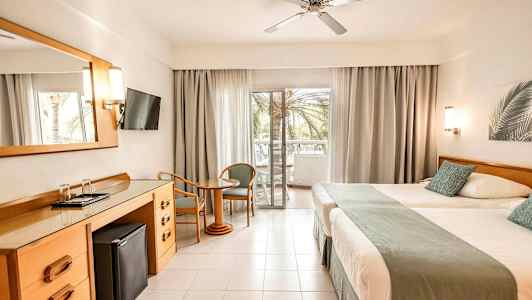 Hotellihuone, jossa kaksi sänkyä, työpöytä, taulutelevisio ja parveke näkymällä. (Tekoälyn luoma teksti)