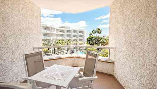 Parveke ulkokalusteilla, näkymä hotellille palmujen ja uima-altaan kanssa. (Tekoälyn luoma teksti)