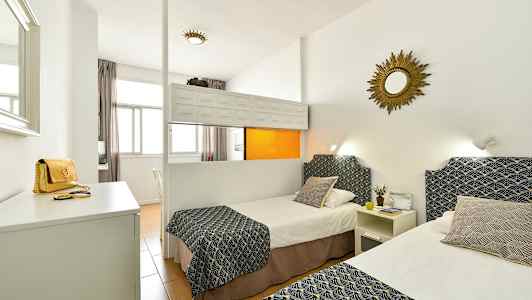 Hotellihuone, jossa on kaksi yksittäistä sänkyä, koristeltuja peitteitä ja tyynyjä, valkoiset seinät ja peili seinällä. (Tekoälyn luoma teksti)