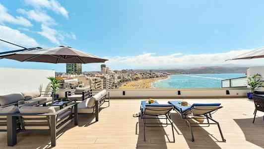 Katoterassi, jossa on huonekaluja, aurinkovarjo ja näkymä rannalle ja merelle. (Tekoälyn luoma teksti)