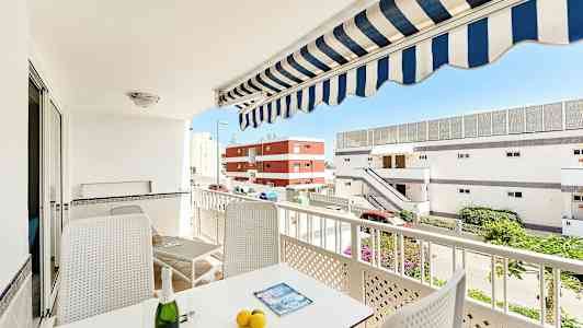 Parveke, jossa on huonekaluja, aurinkovarjo ja näkymä rakennuksiin. (Tekoälyn luoma teksti)