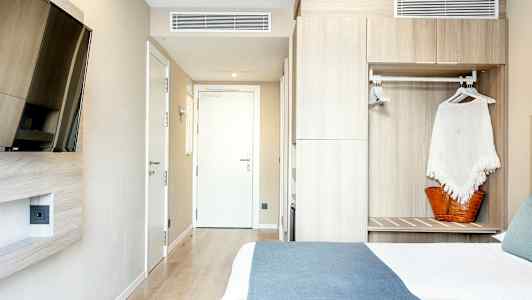 Hotellihuone, jossa sänky, seinään kiinnitetty televisio ja kaappi. (Tekoälyn luoma teksti)