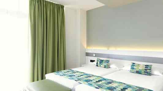 Hotellihuone, jossa kaksi erillisvuodetta, vihreät verhot ja yhteensopivat sängyn koristeet. (Tekoälyn luoma teksti)