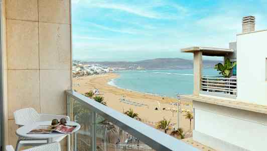 Parveke, jossa on pöytä ja tuolit, tarjoaa näkymän hiekkarannalle ja merelle. (Tekoälyn luoma teksti)