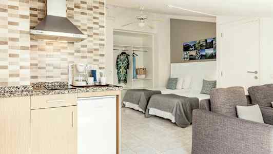 Avoin hotellihuone, jossa on keittokomero, vuoteet ja istuimet. (Tekoälyn luoma teksti)