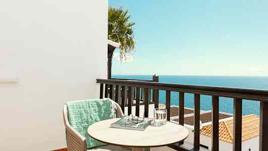 Näkymä parvekkeelta merelle, tuoli, pöytä ja vihreä viltti. (Tekoälyn luoma teksti)