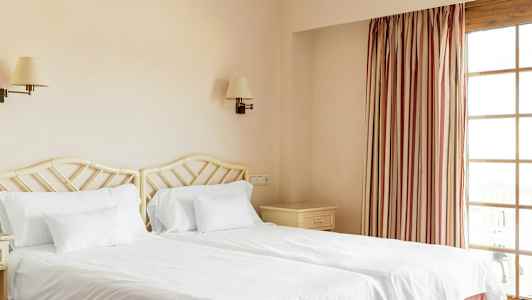 Kaksi yhden hengen vuodetta valkoisilla vuodevaatteilla hotellihuoneessa. (Tekoälyn luoma teksti)