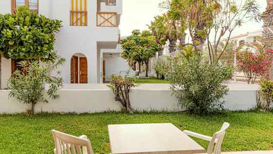 Ulkokalusteet, pöytä ja tuolit, vihreän nurmikon ja valkoisten rakennusten edessä. (Tekoälyn luoma teksti)