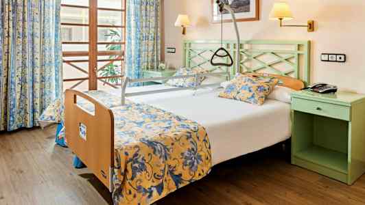 Hotellihuone, jossa on tukikahvalla varustettu sänky ja keltaiset kukkakuvioiset vuodevaatteet. (Tekoälyn luoma teksti)