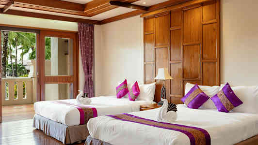 Kaksi vuodetta valkoisilla vuodevaatteilla ja koristetyynyillä huoneessa, jossa on puuyksityiskohtia ja parveke, jolta on näkymä puille. (Tekoälyn luoma teksti)