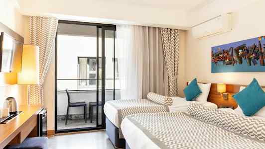 Hotellihuone, jossa on kaksi yhden hengen sänkyä, parveke kalusteineen ja työpöytä lampulla ja vedenkeittimellä. (Tekoälyn luoma teksti)