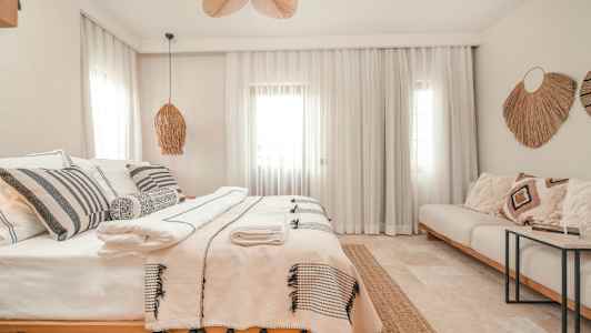 Vaalea ja tyylikäs makuuhuone, jossa on parivuode, koristeellisia tyynyjä ja tekstiilejä. (Tekoälyn luoma teksti)