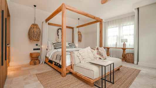 Makuuhuone, jossa on puurunkoiset pylvässängyt, koristeelliset tyynyt ja vaalea sisustus. (Tekoälyn luoma teksti)