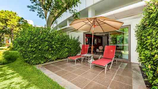 Terassi, jossa kaksi punaista aurinkotuolia, aurinkovarjo ja vehreä ympäristö. (Tekoälyn luoma teksti)