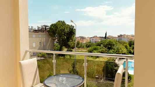 Näkymä parvekkeelta, jossa on pöytä ja tuolit, kohti vehreyttä ja asuinaluetta. (Tekoälyn luoma teksti)